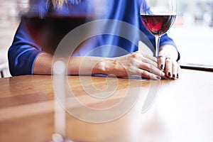 Woman is drinking red wine and having rest in cafe near window, close-up of womanÃ¢â¬â¢s hands holding glass on table